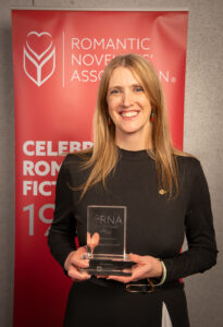 Woman in black dress holding RNA award, long blonde hair