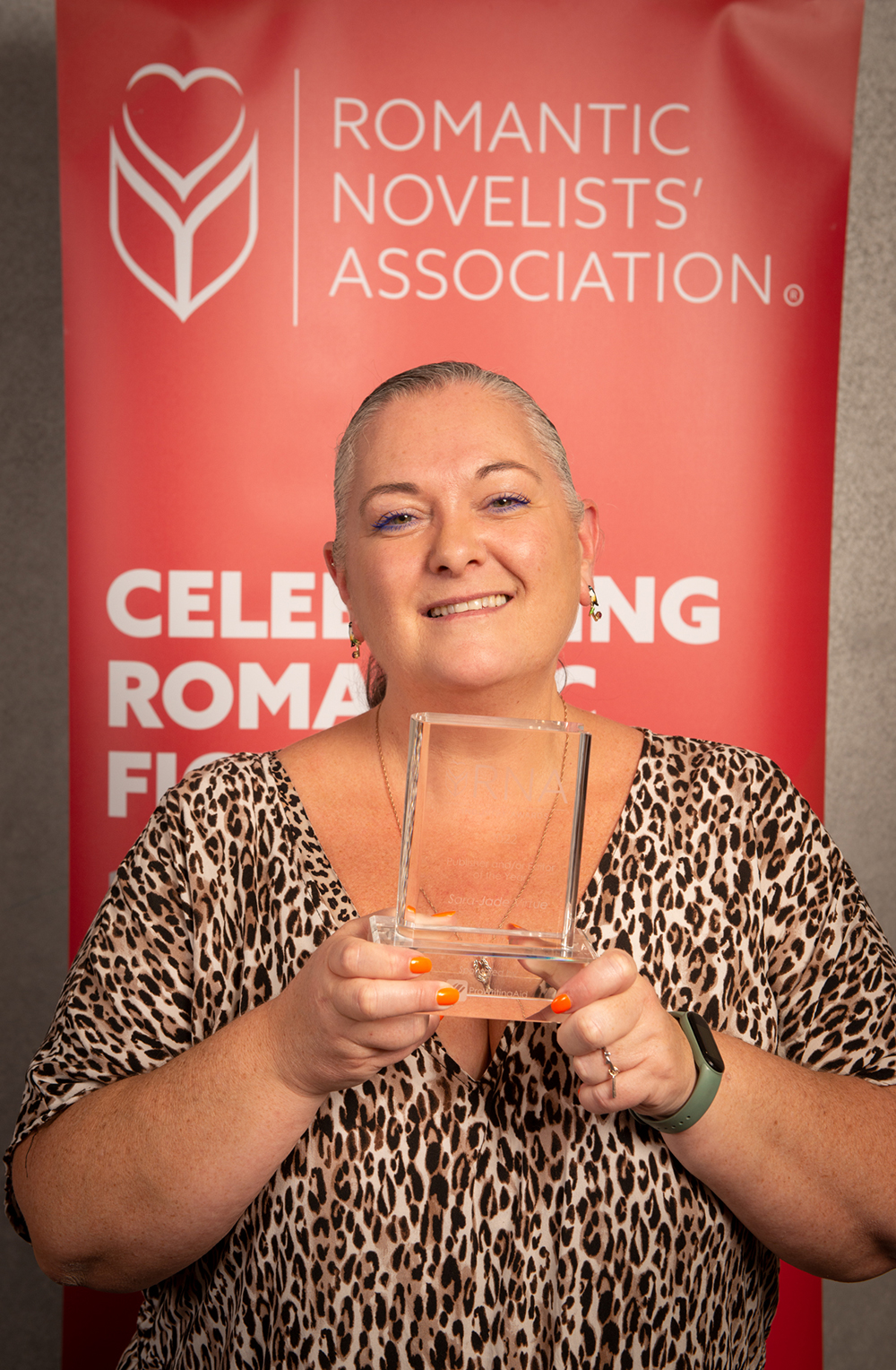 Woman  in leopard print dress holding  glass RNA  award