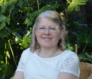 Photo of Linda Corbett, author, wearing a white shirt with green plants behind her