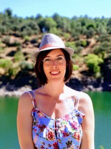 Author Sarah Callejo wearing a sundress and hat near a sunny lake