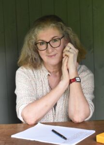 Portrait of author Debbie Young, blonde woman in cream shirt wearing watch and glasses