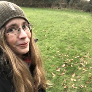Woman with long blonde hair, glasses and hat outside in green space