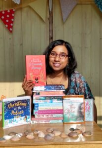 Author Jeevani Charika with her books. Author has dark bobbed hair and glasses and is pictured with a pile of her books. 