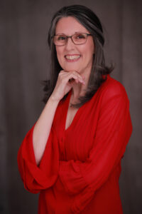 picture of Laura James, author, wearing a bright red top and glasses, medium length dark hair, big smile