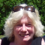 Woman with white hair, sunglasses on head, black top, smiling, sunburn