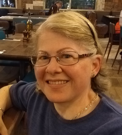 A photo of Linda. She has blonde hair and glasses, and is smiling.