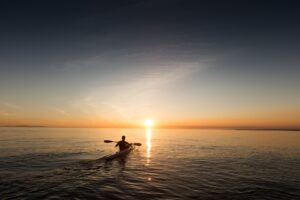 Person canoeing towards sunset