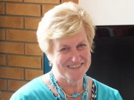 A photograph of Ros Rendle -she has short blonde hair and a smile, and is wearing a turquoise top with matching necklace.