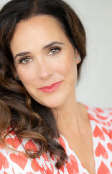 Author Julia Boggio. Woman with dark brown hair, smiling, brown eyes, dress with hearts on it